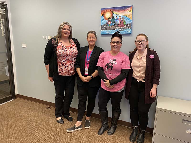 Four women stand in a row wearing pink shirts to show support for Pink Shirt Day 2020