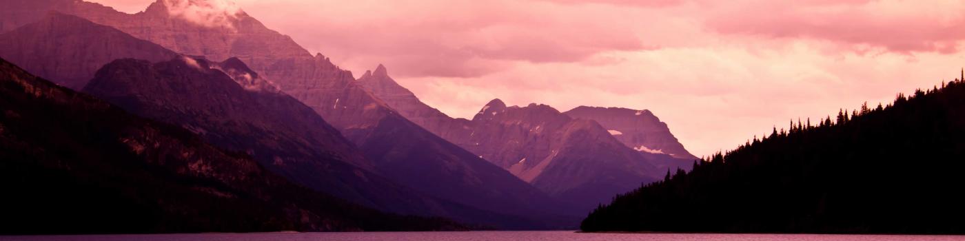 Cloudy sun setting over mountain range and lake